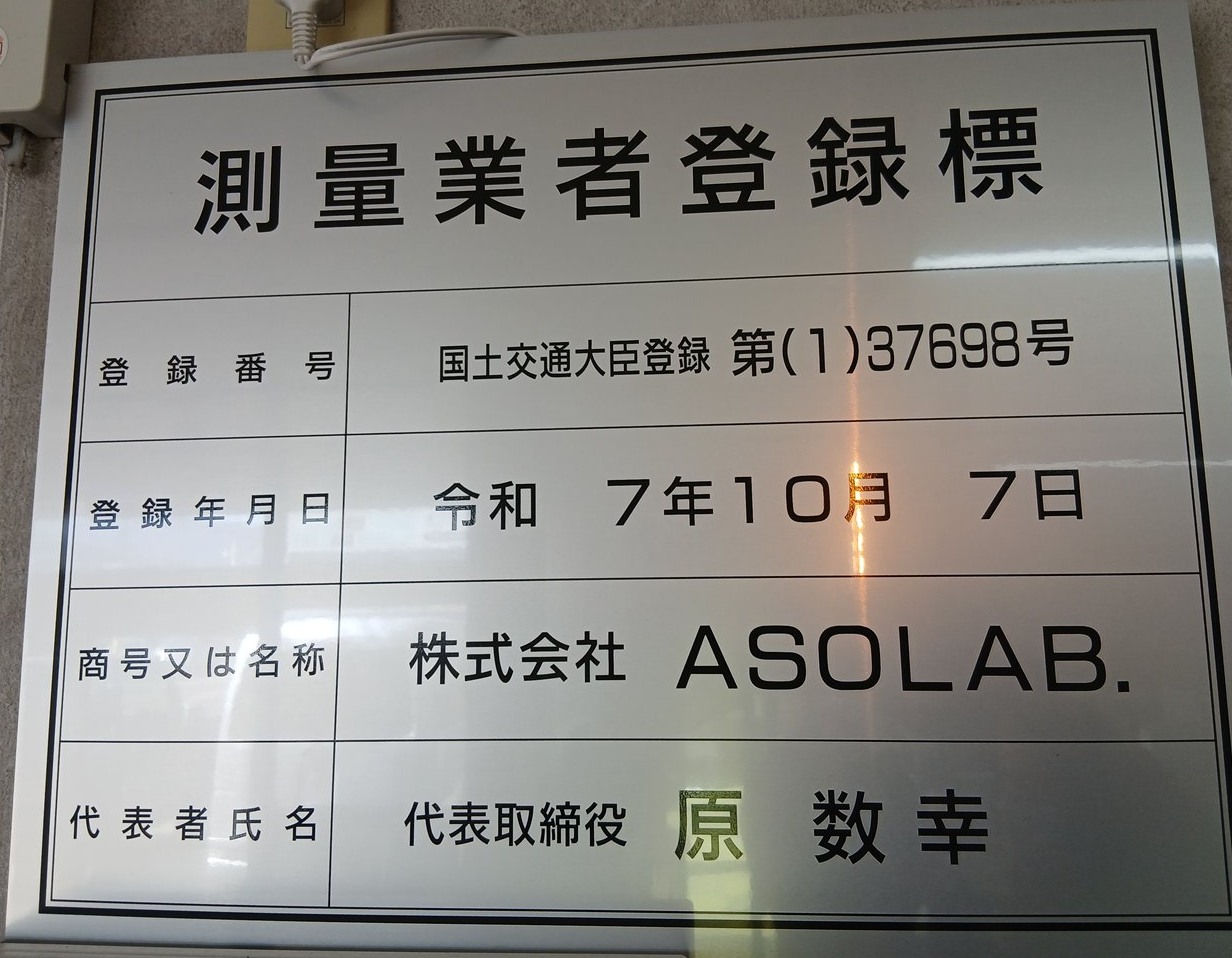 事務所に掲示している測量業者登録標。国土交通大臣登録 第(1)37698号、登録年月日 令和7年10月7日、商号 株式会社ASOLAB.、代表取締役 原 数幸と記されている
