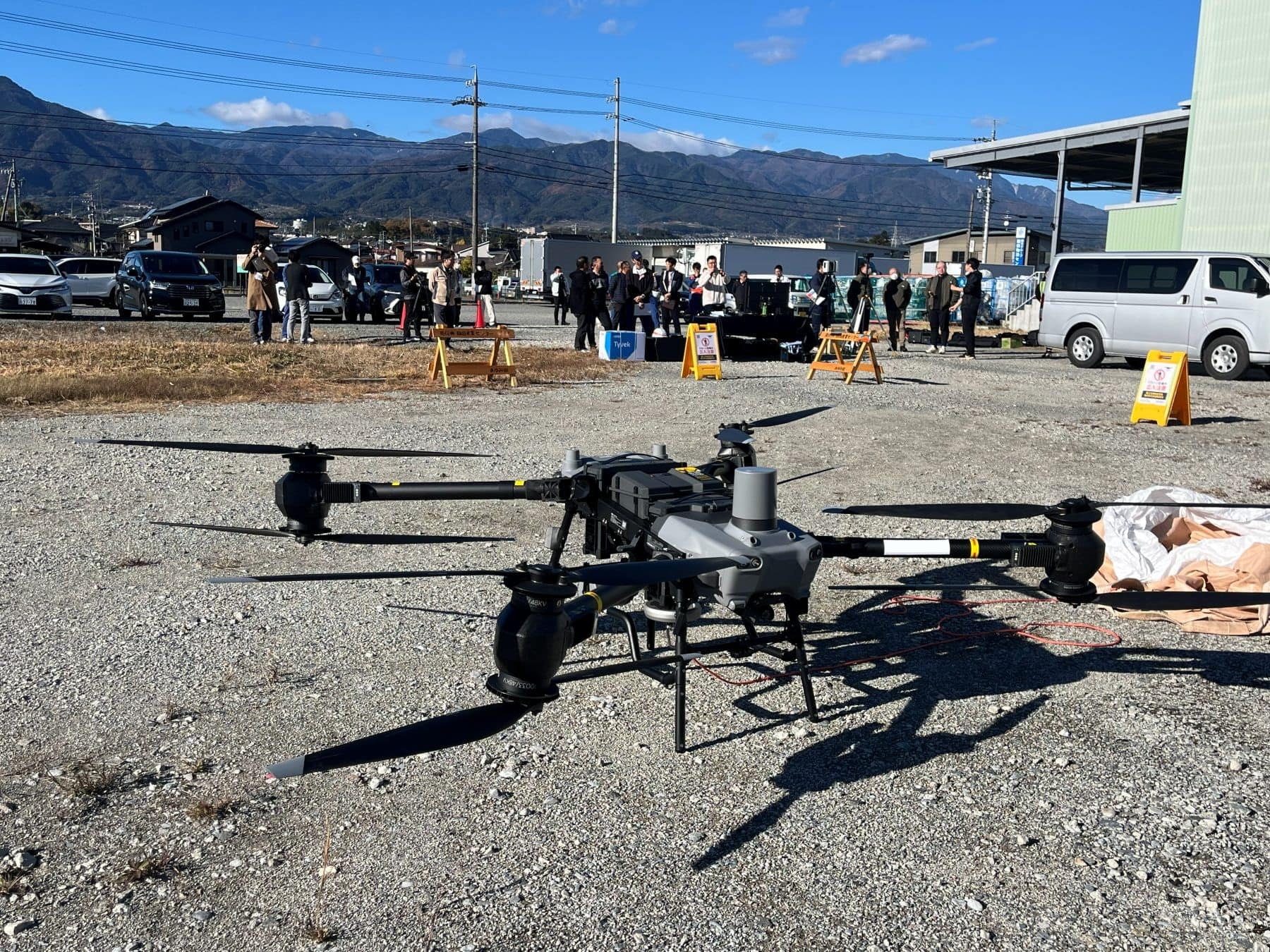 屋外の会場に置かれた物流ドローンと、その奥で説明を聞く見学者