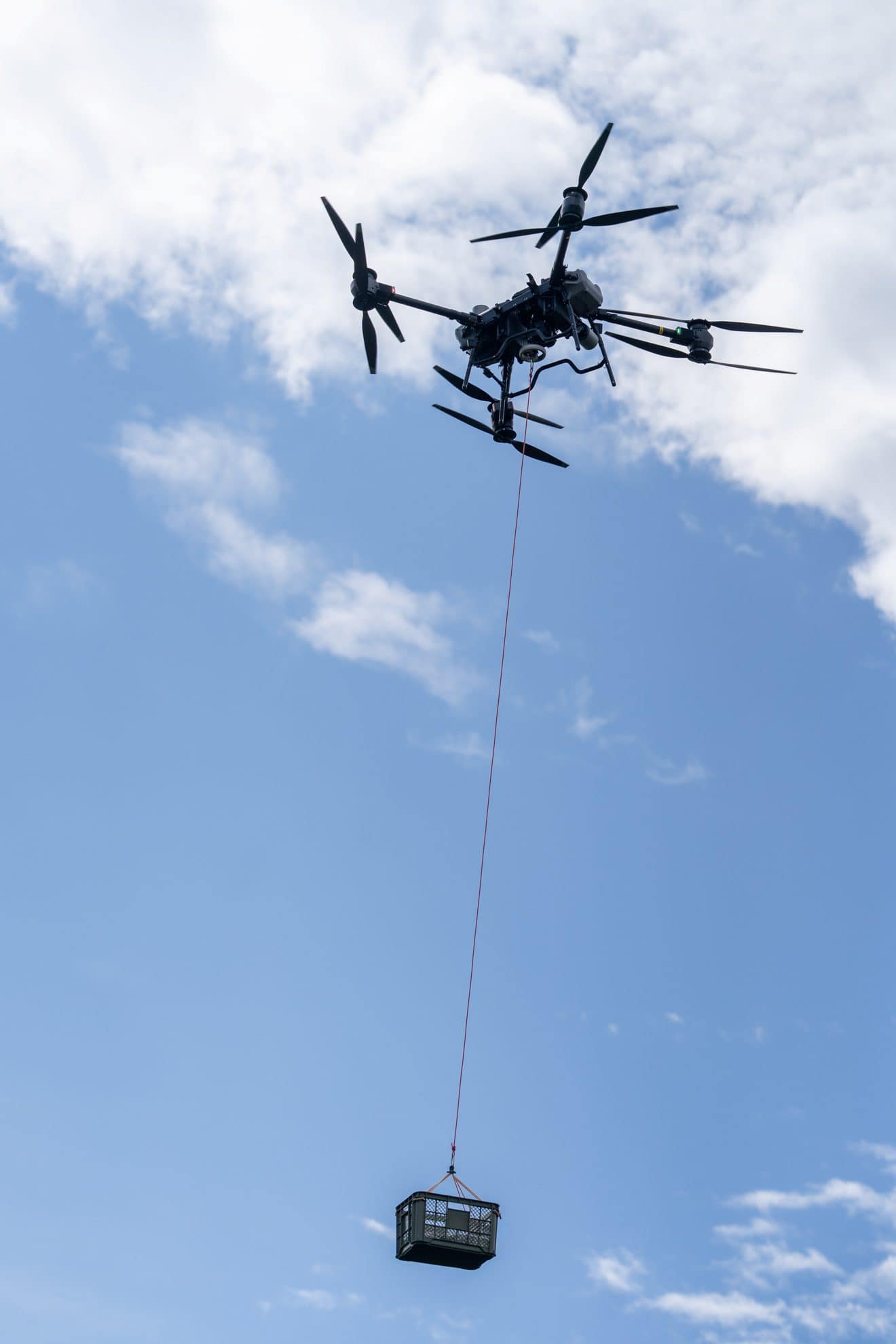 青空の下、ロープでコンテナを吊り下げて飛ぶ FlyCart 30
