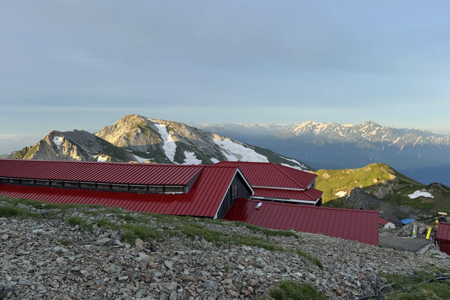 朝日に照らされた北アルプスの山並みと、稜線に建つ赤い屋根の山小屋