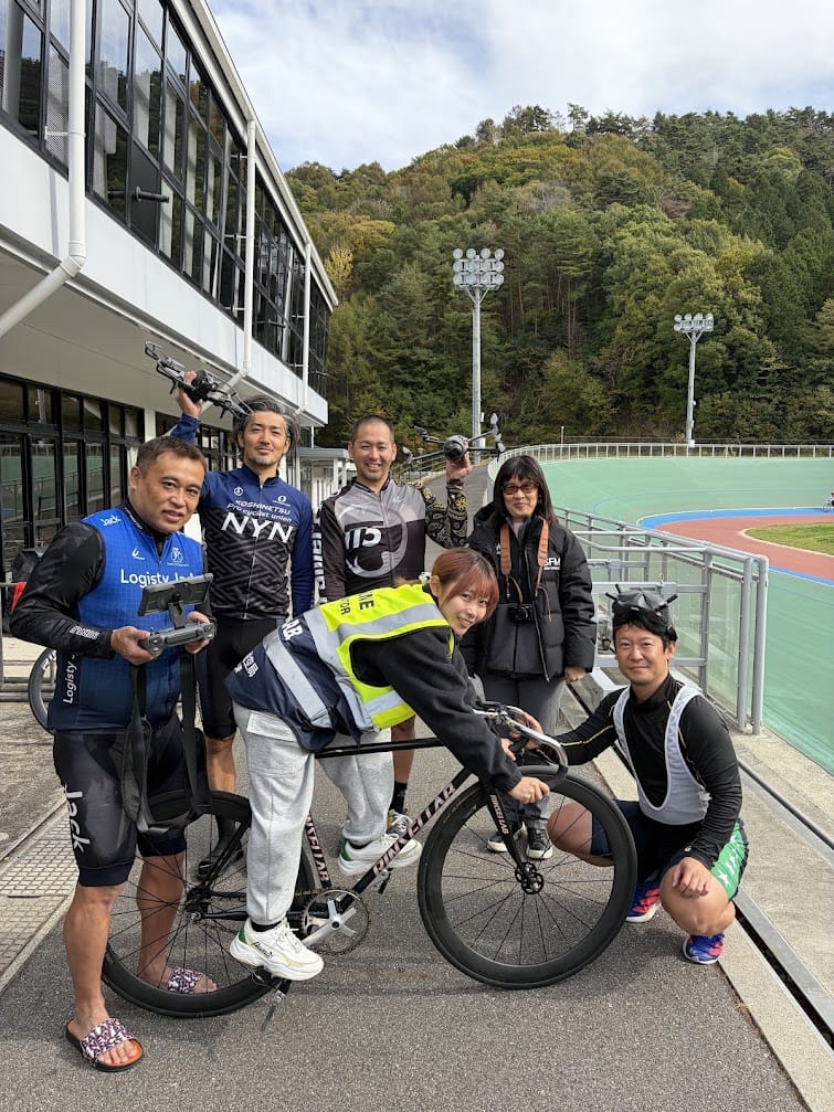 競技場の前で、ドローンを掲げて記念撮影する選手と当社スタッフ