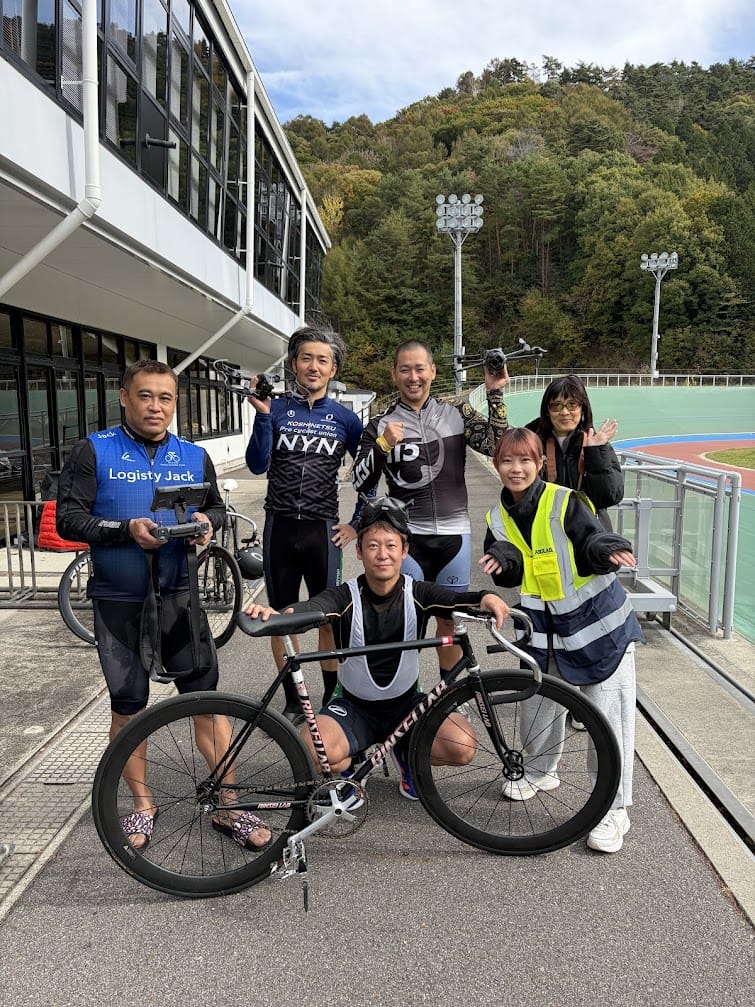 自転車とドローンを手に並ぶ自転車競技の選手と当社スタッフ