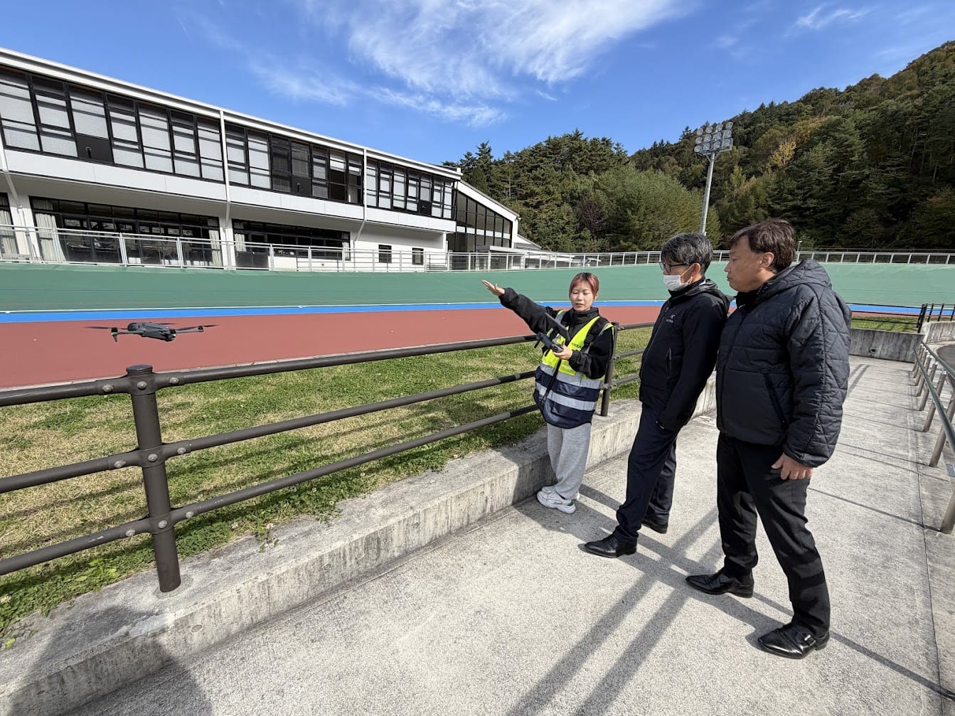 飛行中のドローンを示しながら、松本市の職員に撮影内容を説明する当社のドローン操縦者