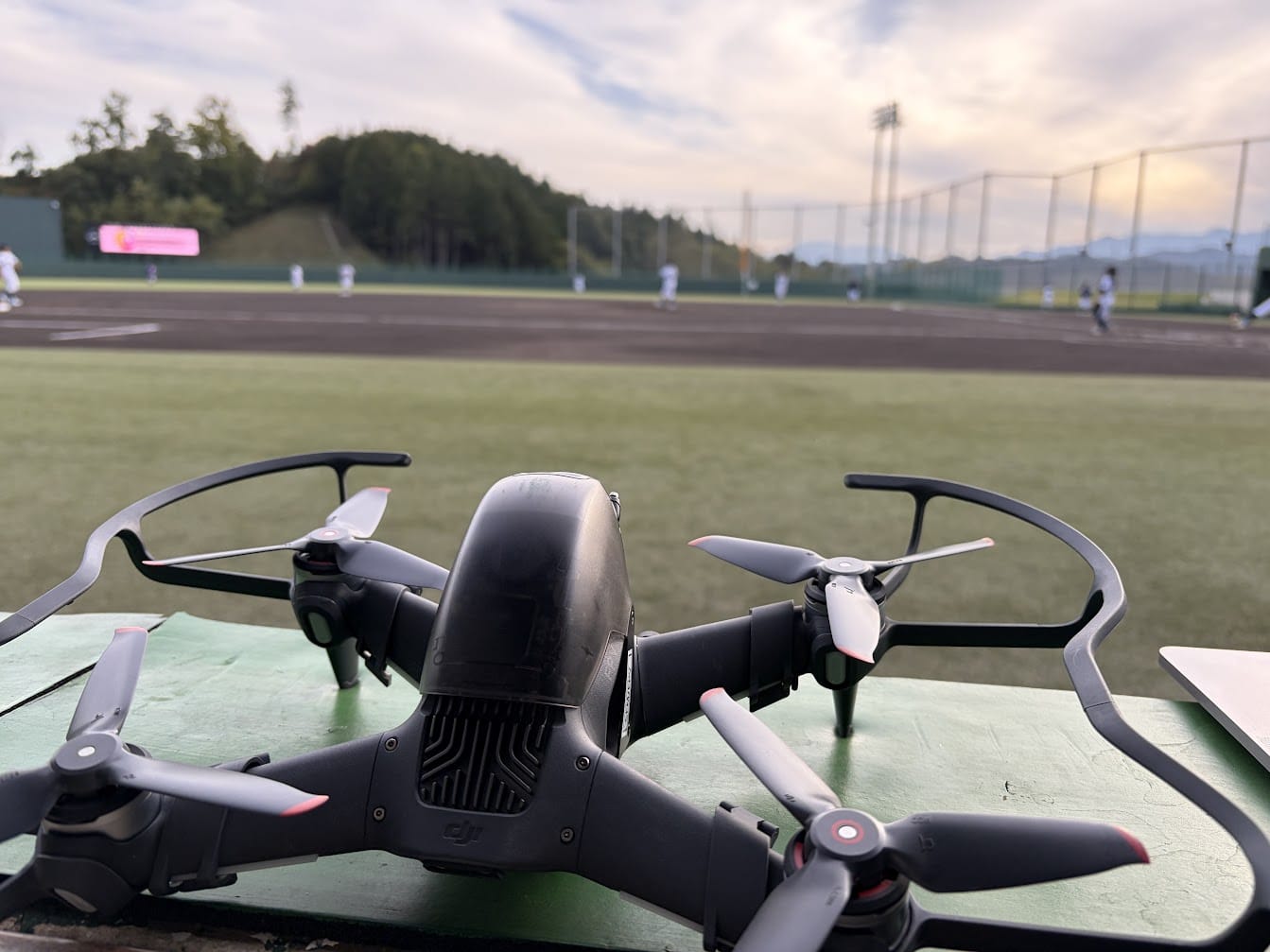 球場のベンチ前に置いたDJI FPVと、奥で練習する選手たち