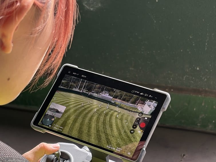 DJI Mavic 4 Proの送信機の画面で、外野の映像を確認する当社スタッフ